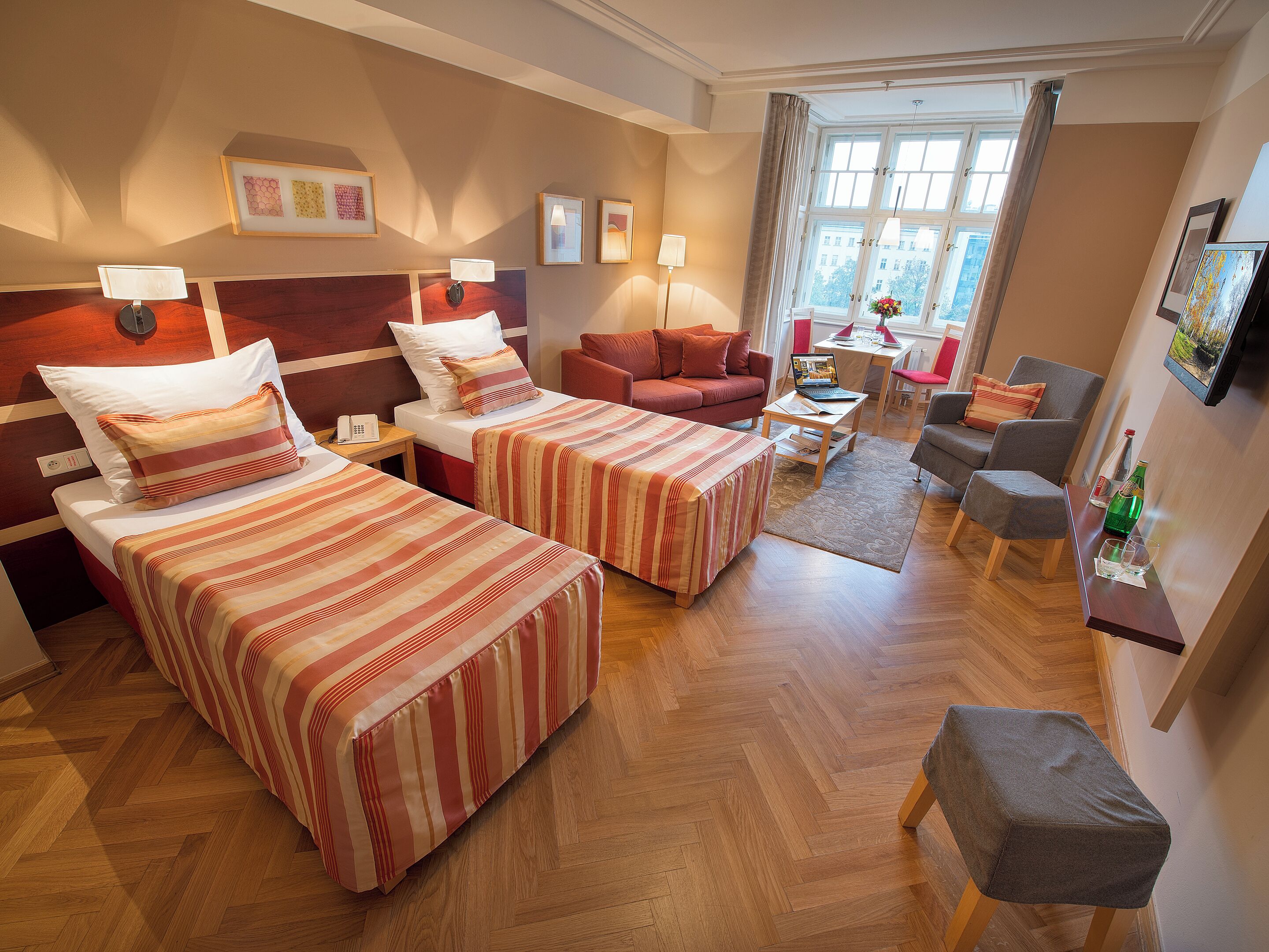 Una camera d'albergo con due letti, un divano, una scrivania e una televisione.