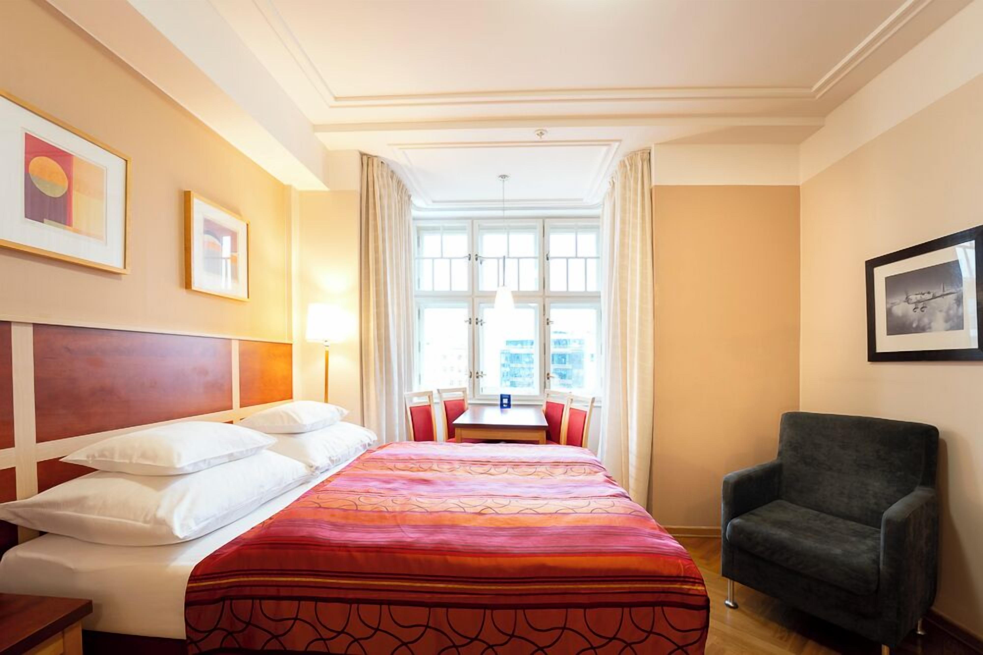A hotel room with a bed, a chair, a table, and a window with curtains.