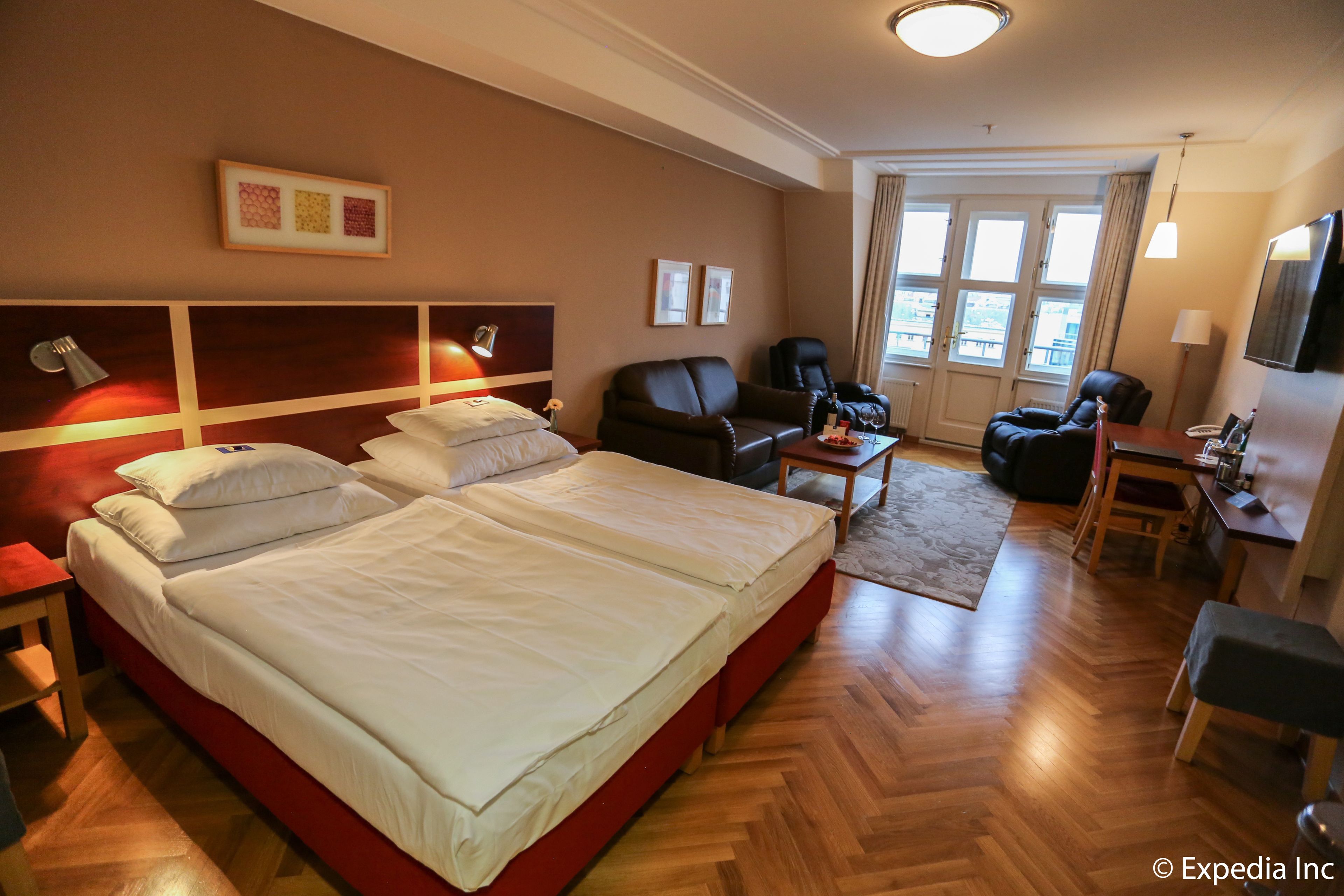 A hotel room with a large bed, a desk, a chair, and a sofa.