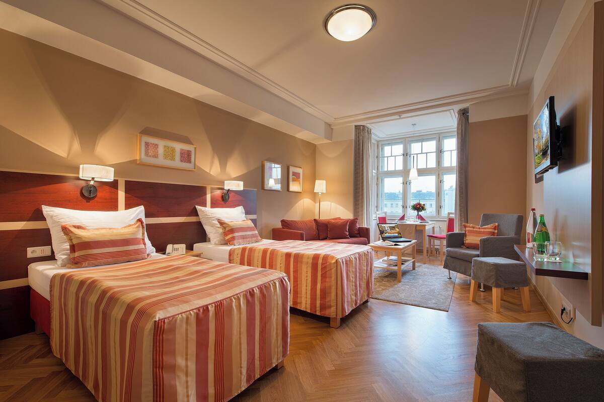 A hotel room with two beds, a desk, a chair, and a TV.