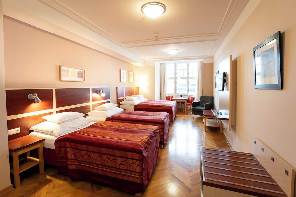 A hotel room with four beds, a desk, a chair, and a window.
