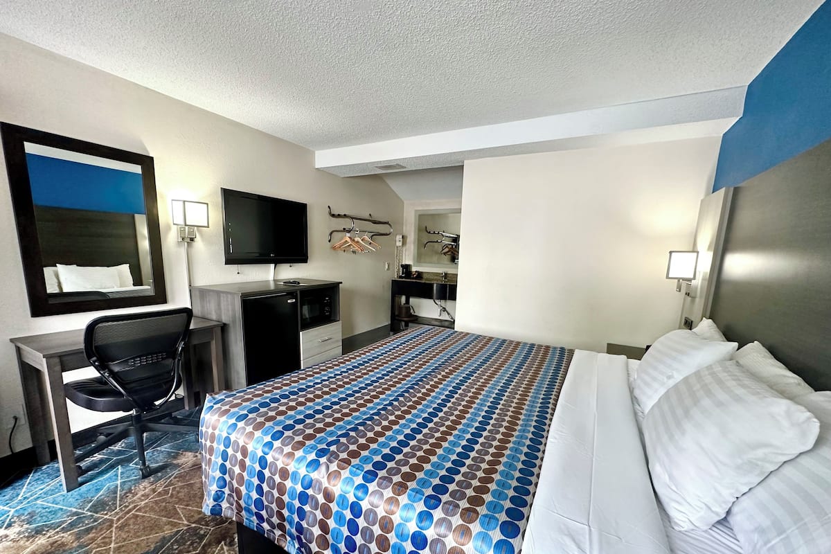 A hotel room with a bed, a desk, a chair, a TV, and a mirror.