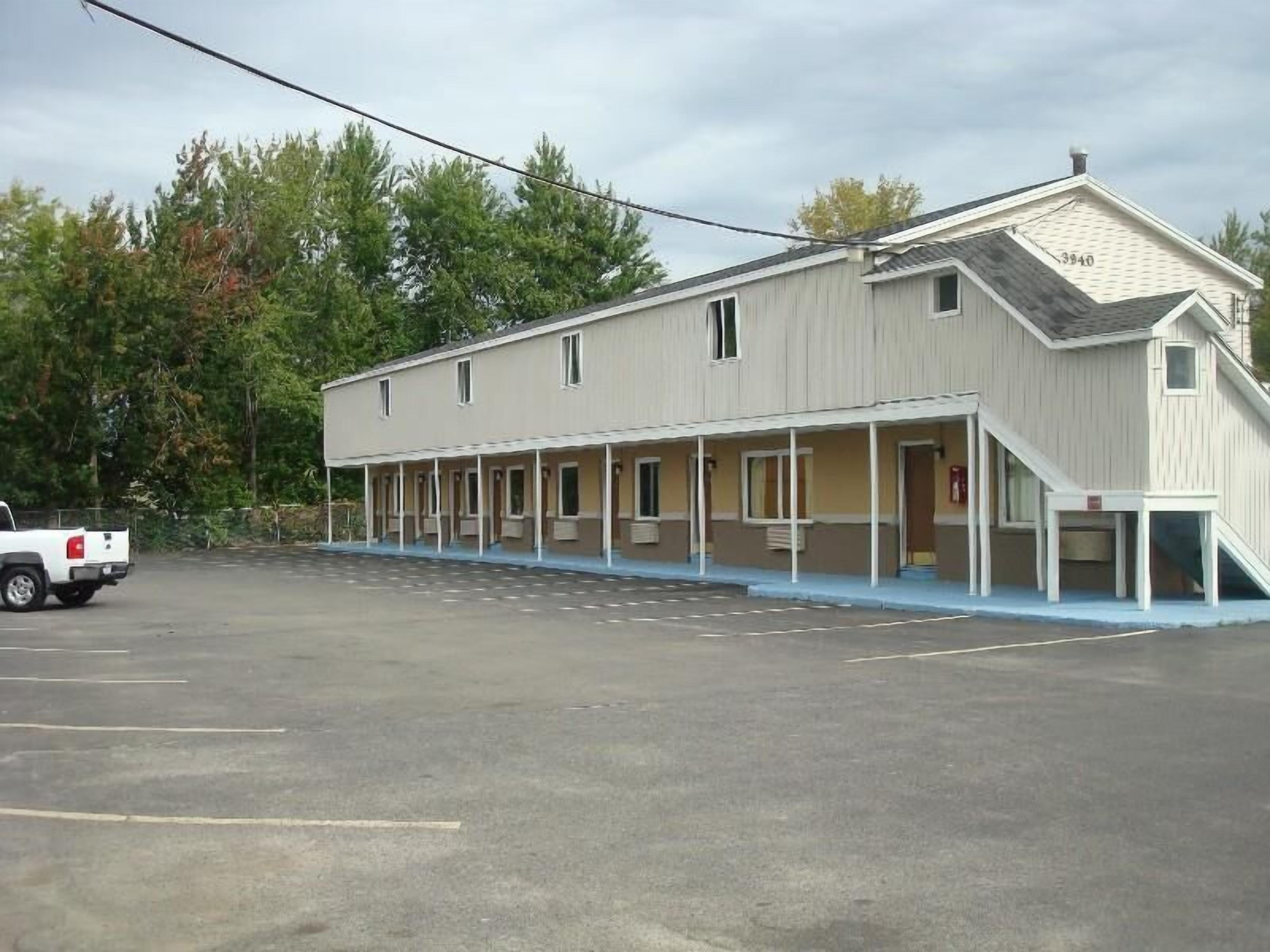 Un motel con área de estacionamiento techada y un edificio de un piso con techo plano.