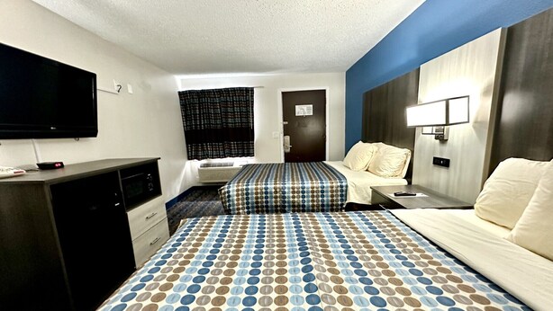 A hotel room with a large bed, a desk, a flat-screen TV, and a window with curtains. - Red Carpet Inn Orchard Park - Buffalo, NY (Orchard Park)