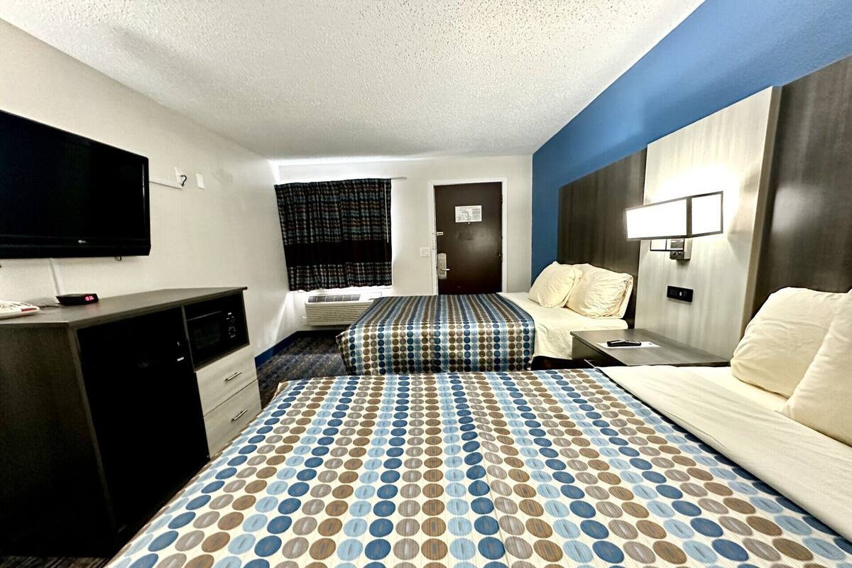 A hotel room with a large bed, a desk, a flat-screen TV, and a window with curtains.