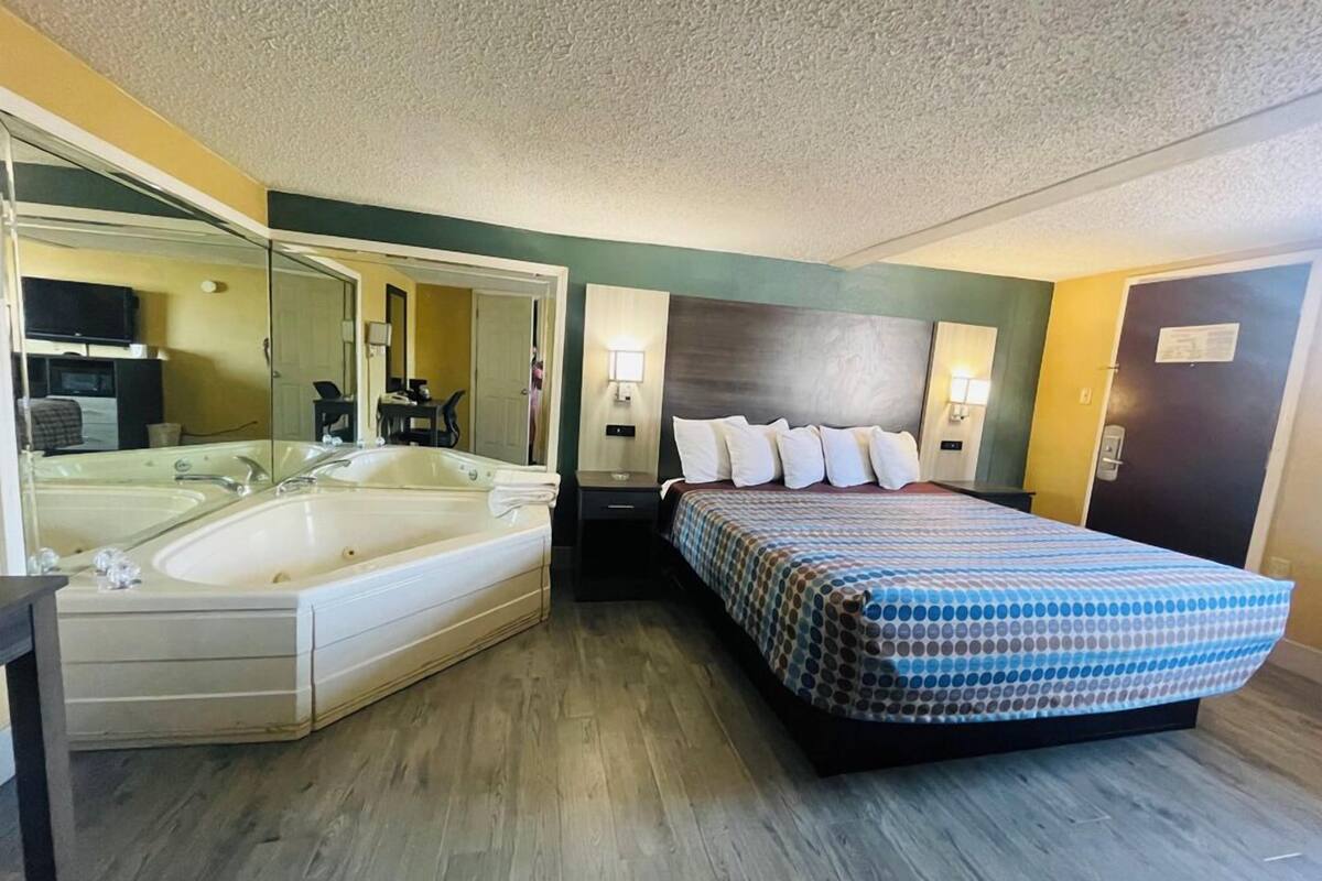 A hotel room with a large bed, a separate bathtub, a mirror, and a small desk.