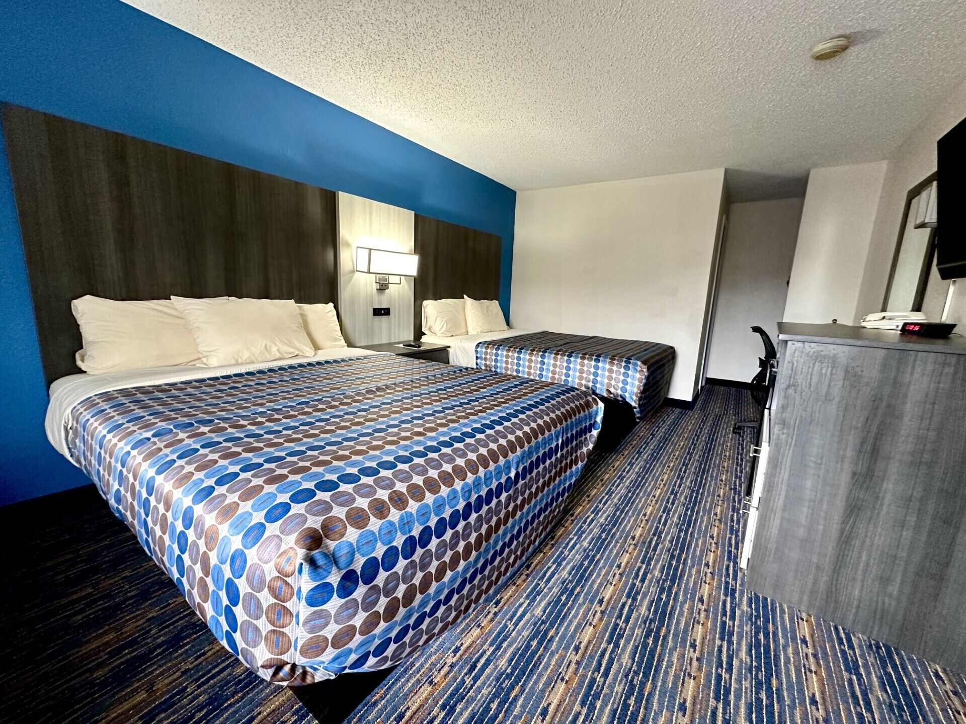 A hotel room with two beds, a desk, and a TV.