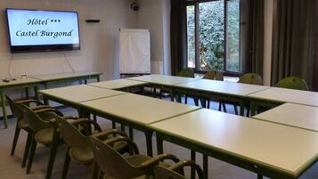 A conference room with a long table and chairs, a projector screen displaying 'Hôtel *** Castel Bourgond', a whiteboard, and a window with a view of greenery.
