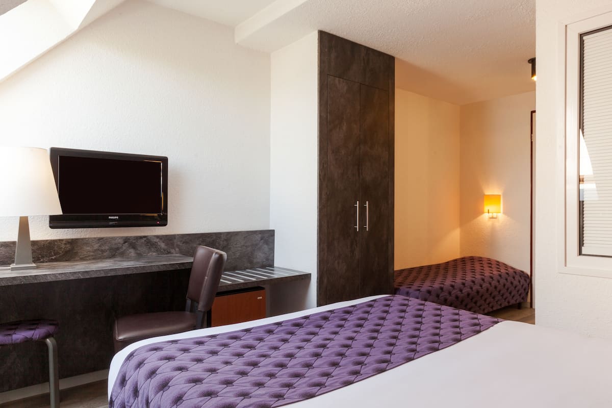 A hotel room with a bed, a desk with a chair, a television, and a wardrobe.