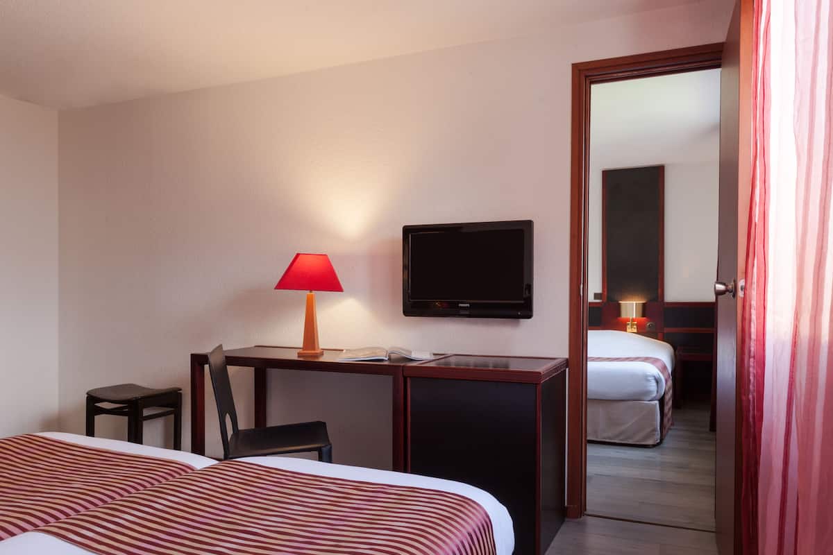 A hotel room with two beds, a desk with a chair, a television, and a door leading to another room.
