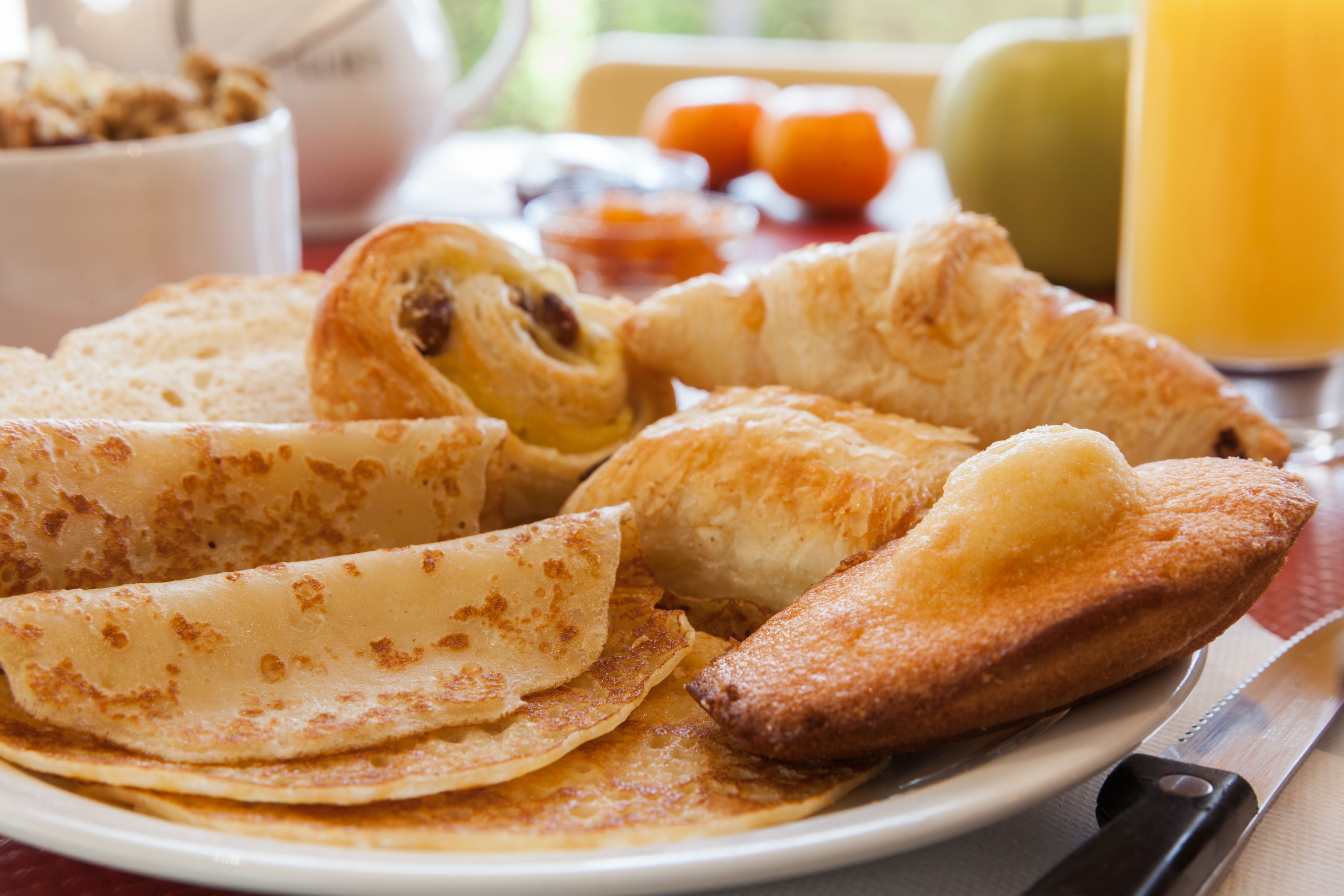 Une assiette de crêpes, accompagnée d’un couteau et d’un verre de jus d’orange.