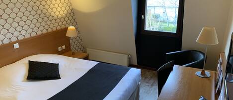 A hotel room with a bed, a nightstand, a desk with a coffee maker, and a window.