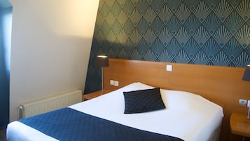 A hotel room with a bed, a headboard, a wall with a geometric pattern, and a nightstand with a lamp.