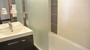 A modern bathroom with a glass shelf holding toiletries, a white sink, a dark-colored vanity, and a white bathtub.