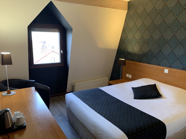 Ett hotellrum med en säng, ett skrivbord med en vattenkokare och koppar, en TV och en vägg med ett mönster.