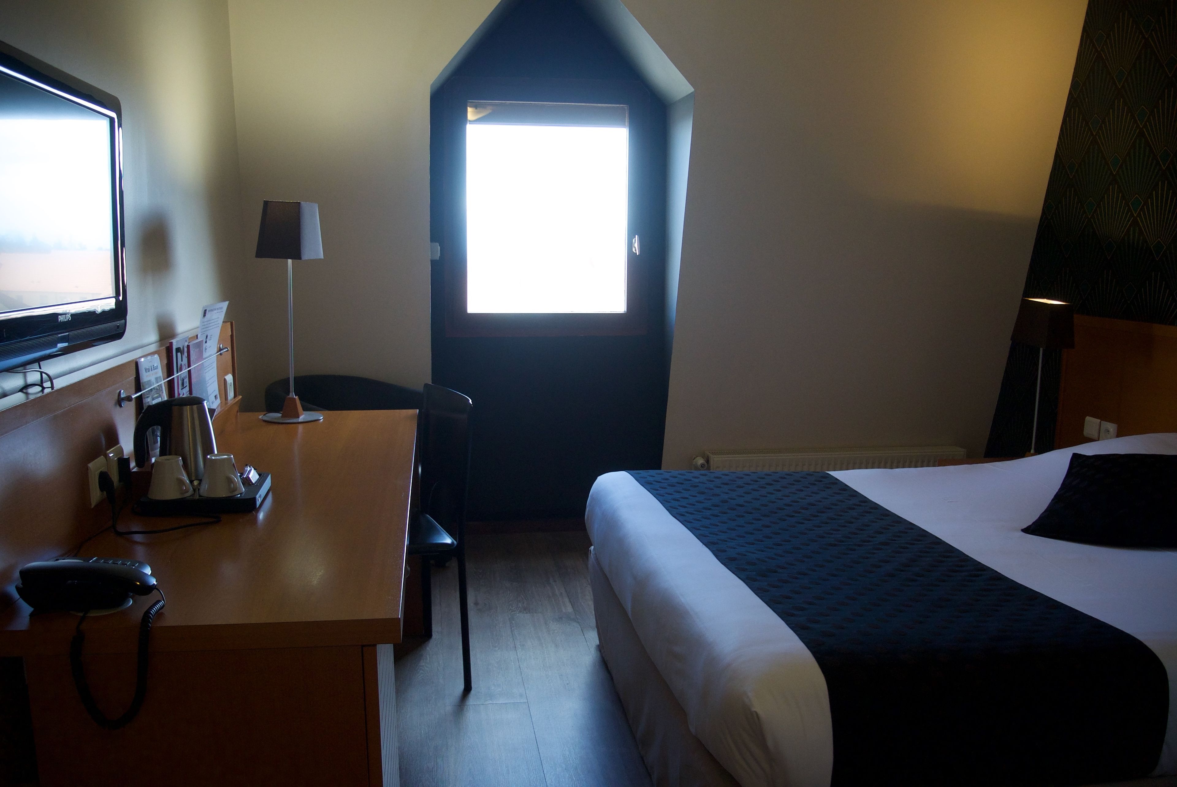 A hotel room with a bed, a desk with a telephone, a lamp, and a TV.