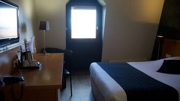 A hotel room with a bed, a desk with a telephone, a lamp, and a TV.