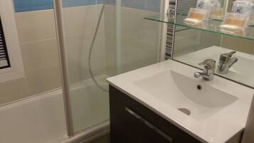A bathroom with a glass shower enclosure, a white sink, and a mirror.