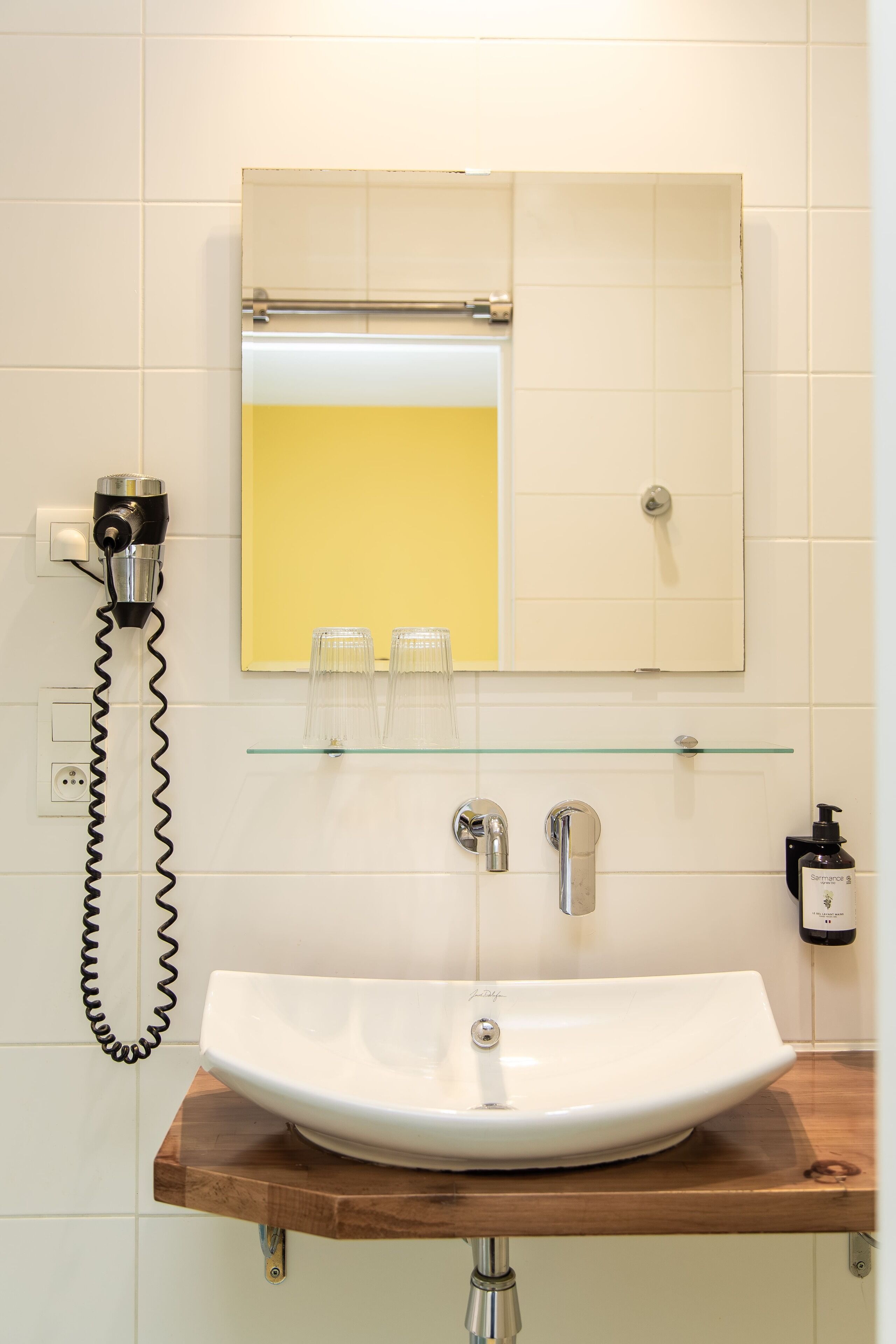 A bathroom with a white sink, a mirror, and a hairdryer on a wall-mounted shelf.