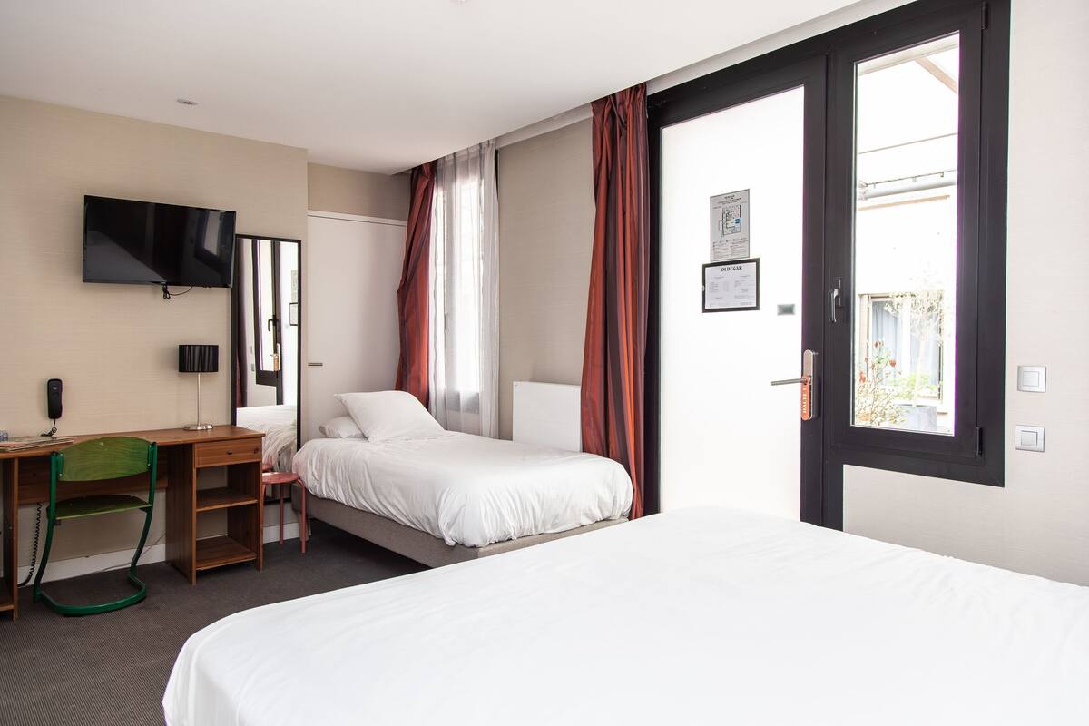 Une chambre d’hôtel avec un lit, un bureau, une chaise, une télévision et une fenêtre avec des rideaux.