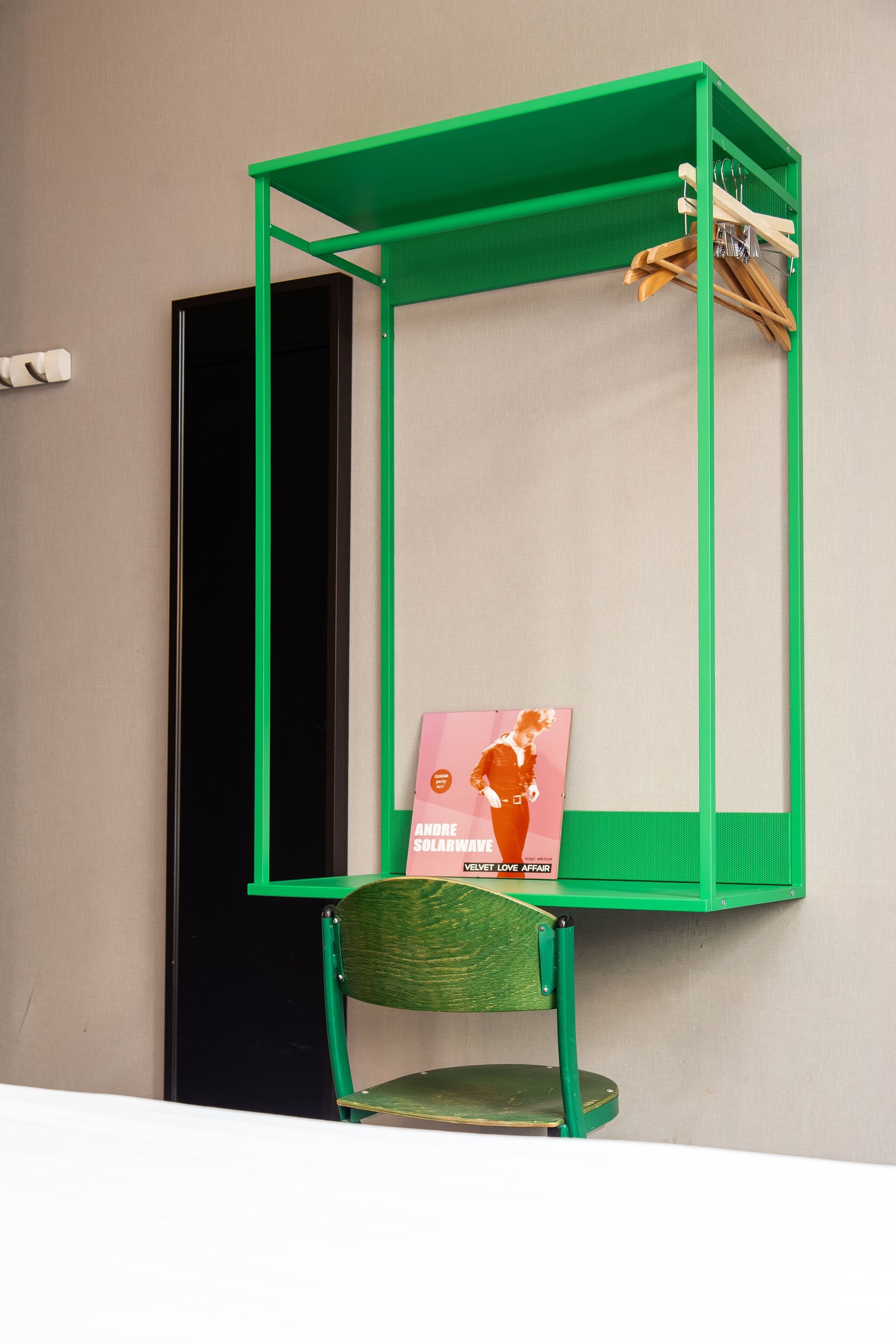 A green metal shelf unit with a chair and a magazine rack against a wall.