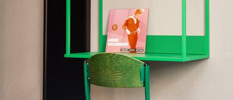 A green metal shelf unit with a chair and a magazine rack against a wall.