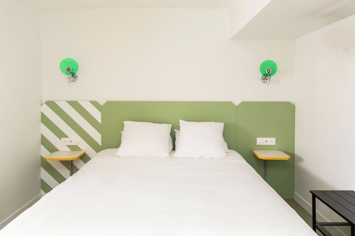 A neatly made bed with two pillows, a green-striped headboard, and two bedside tables with lamps.