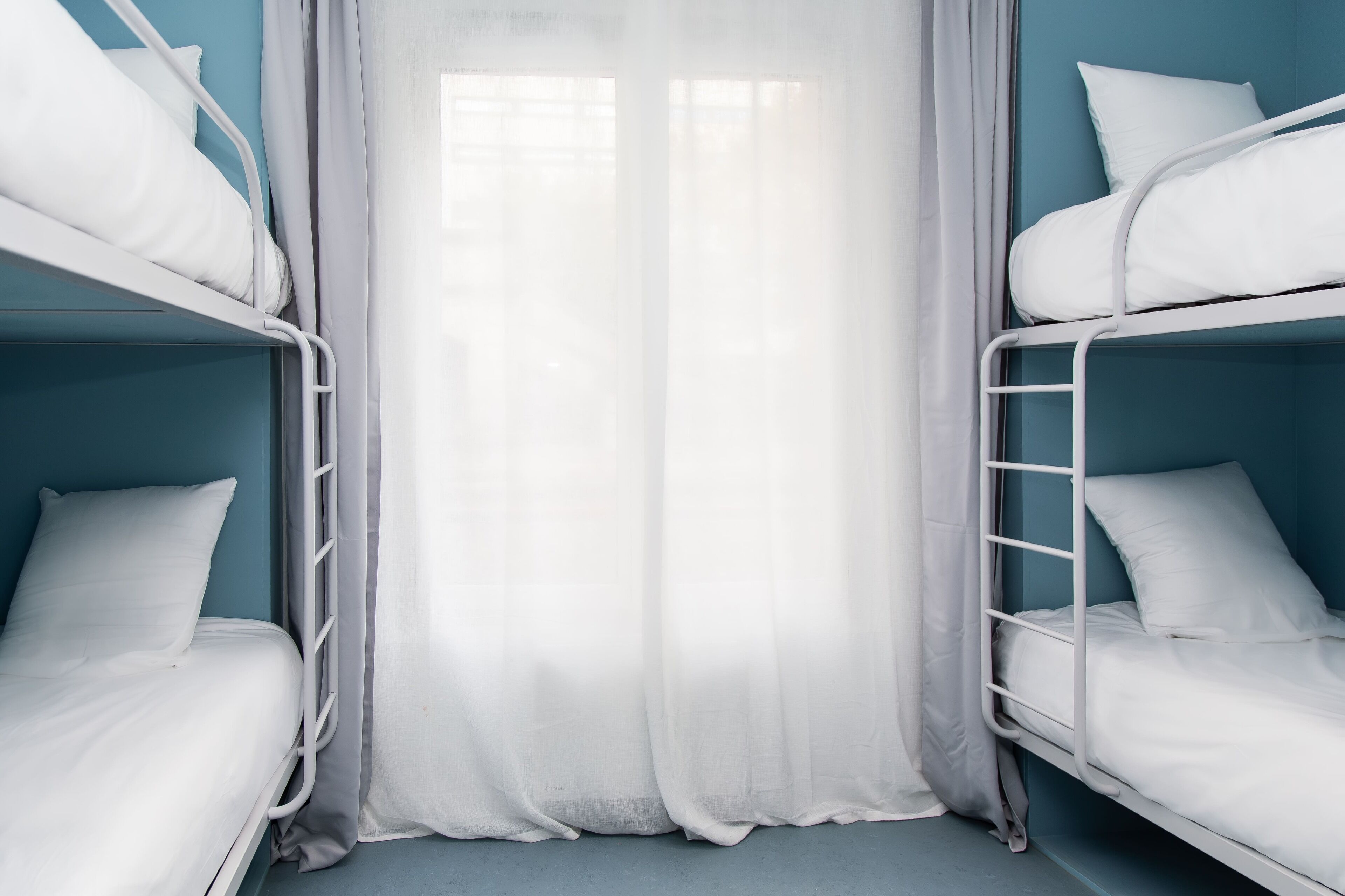 Dormitorio con literas, ropa de cama blanca y cortina translúcida.