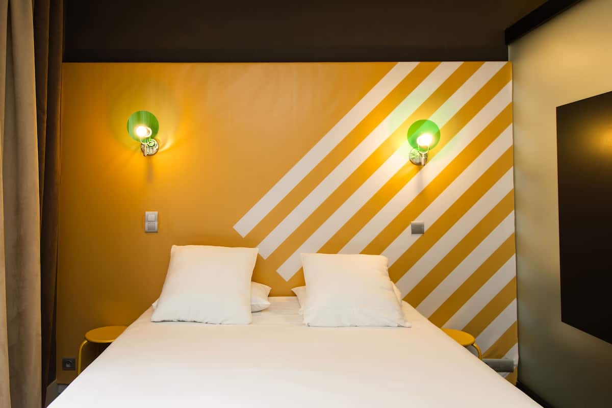 Une chambre d’hôtel comprenant un lit, deux tables de chevet et deux lampes fixées au mur.