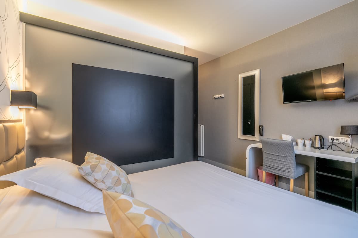 Une chambre d’hôtel moderne dotée d’un grand lit, d’un bureau, d’une télévision à écran plat et d’un miroir fixé au mur.