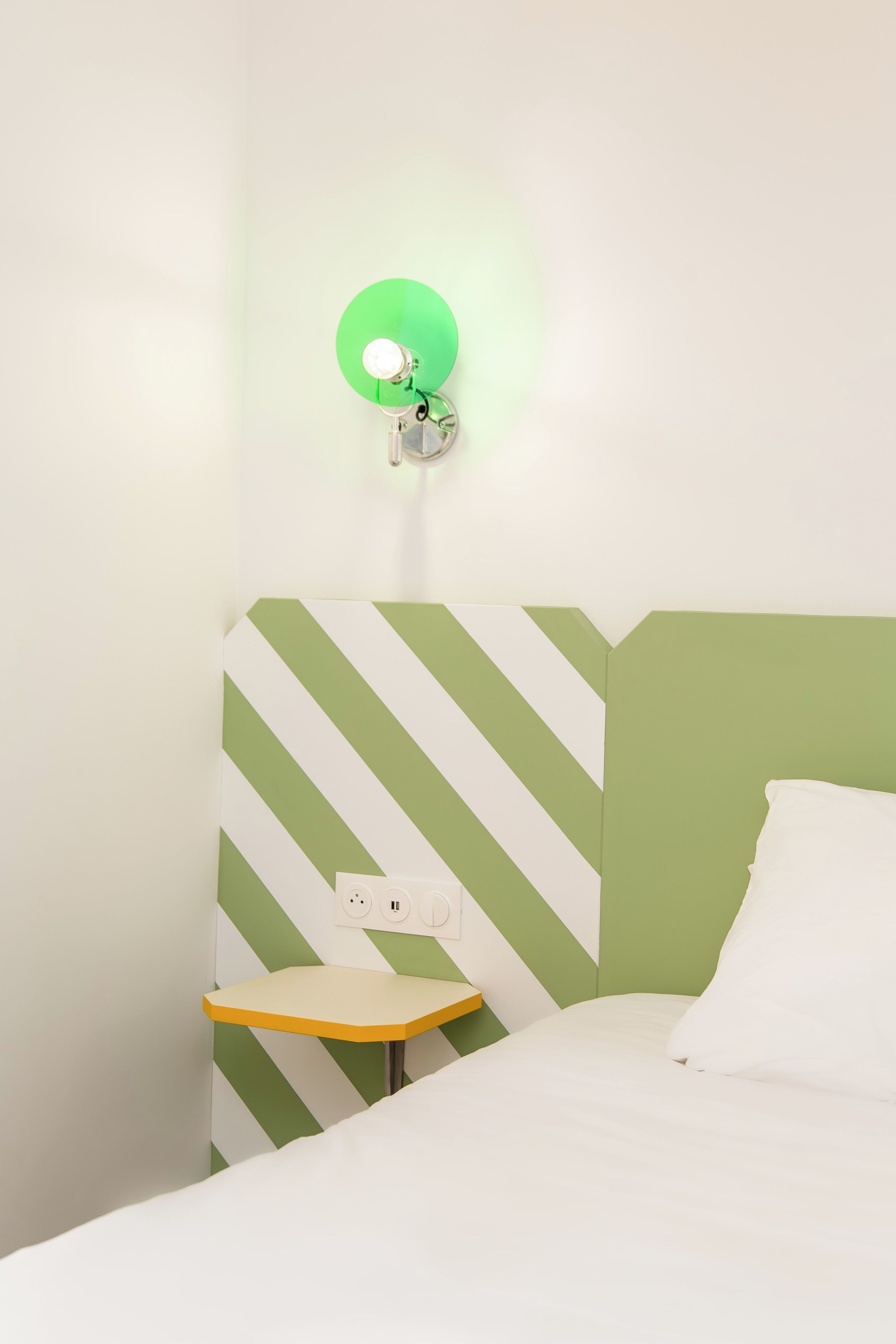 A room with a bed, a nightstand, and a wall-mounted lamp.
