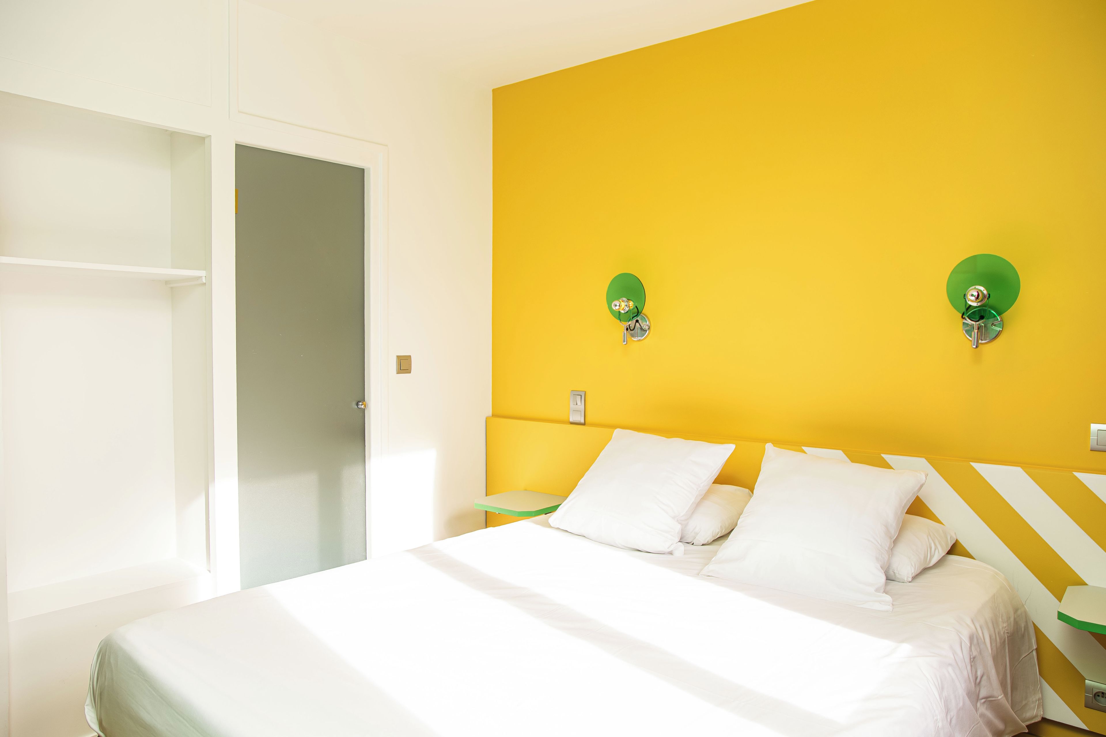 Una habitación con cama, armario y pared amarilla.