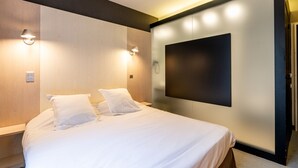 Une chambre d’hôtel moderne dotée d’un grand lit, de deux tables de chevet, d’un téléviseur fixé au mur et d’un éclairage d’ambiance.