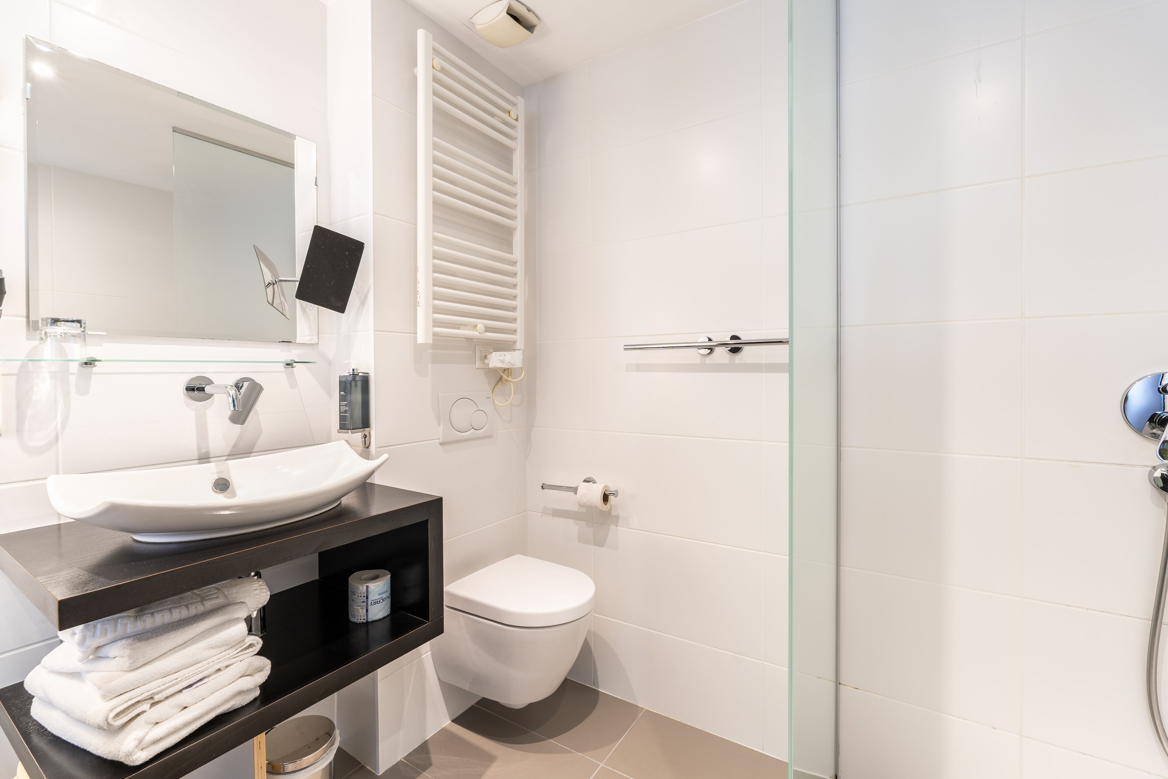 A modern bathroom with a white sink, toilet, and glass shower enclosure.
