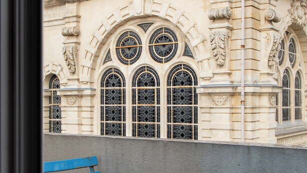 Un bâtiment doté de fenêtres en arc de cercle et d’un balcon avec des chaises et une table bleues.
