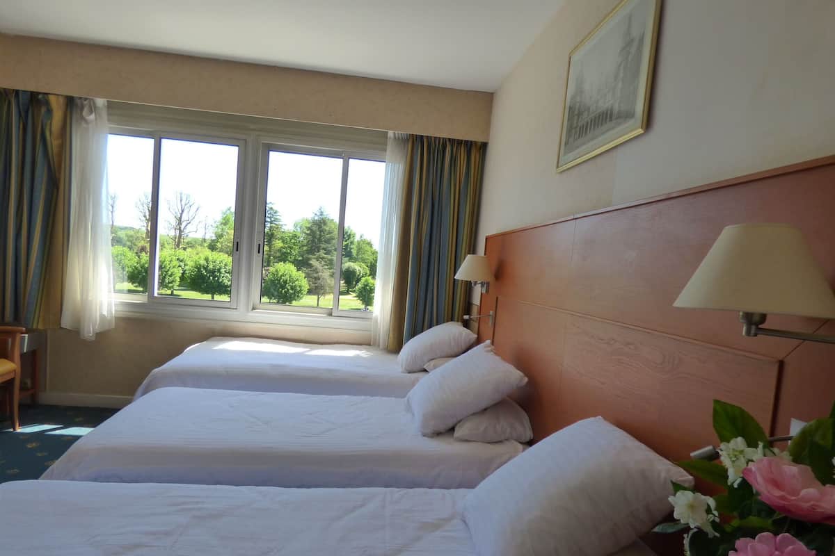 A hotel room with two beds, a window with curtains, a wooden headboard, a lamp, and a framed picture on the wall.