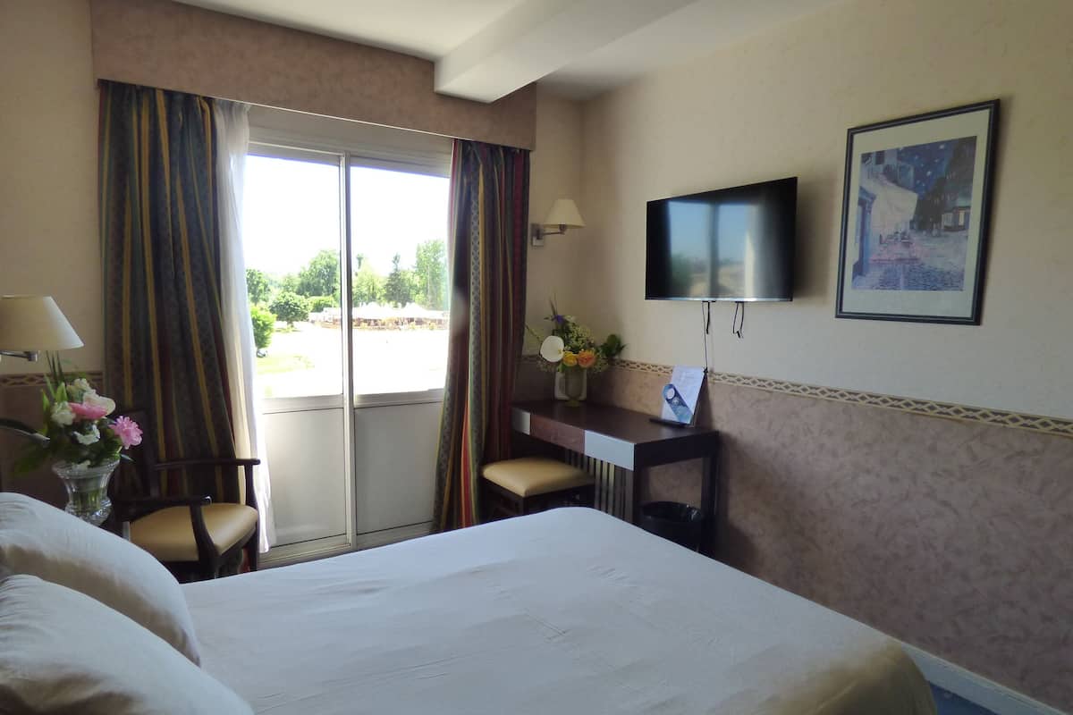 A hotel room with a bed, a desk, a chair, a TV, and a window with curtains.