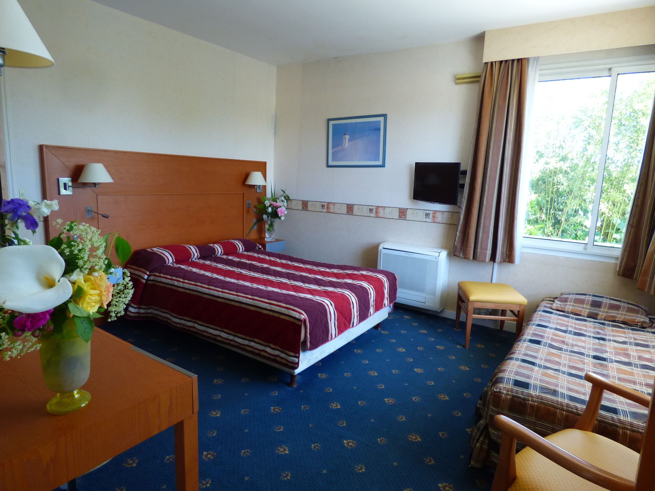 A hotel room with a bed, a desk, a chair, a TV, and a window with curtains.