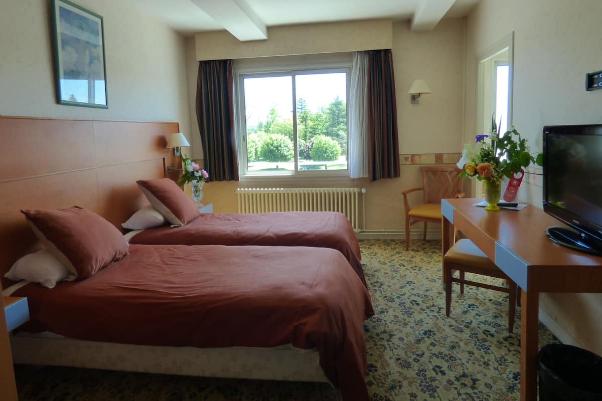 A hotel room with two beds, a desk with a TV, a chair, a window with curtains, and a radiator.
