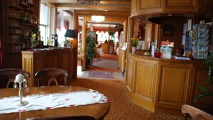 A traditional hotel lobby with wooden paneling, a central seating area with a table, and a bar area with various items on display.