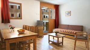 A cozy living room with a wooden dining table, chairs, a sofa, and a television. - Noemys Le Pra Palier (Orcieres)
