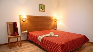 A hotel room with a wooden headboard, two bedside lamps, a red-striped bedspread, a wooden chair, and a small table with a red cloth. - Noemys Le Pra Palier (Orcieres)