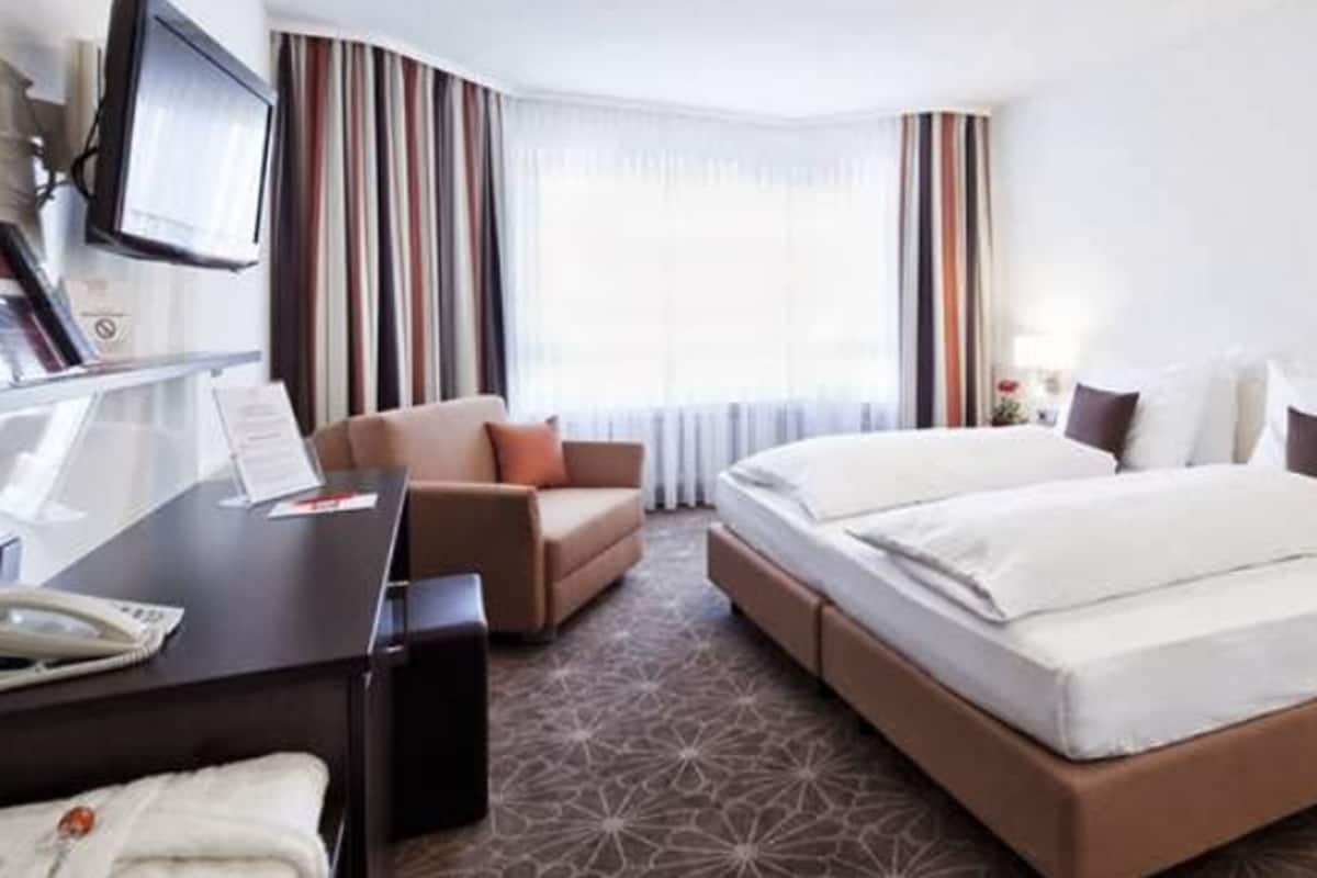 A hotel room with a bed, a desk, a chair, and a television.