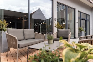 An outdoor seating area with a sofa and chairs, a wooden table, and potted plants. -  ZELLER's Quartier (Koenigsbrunn)