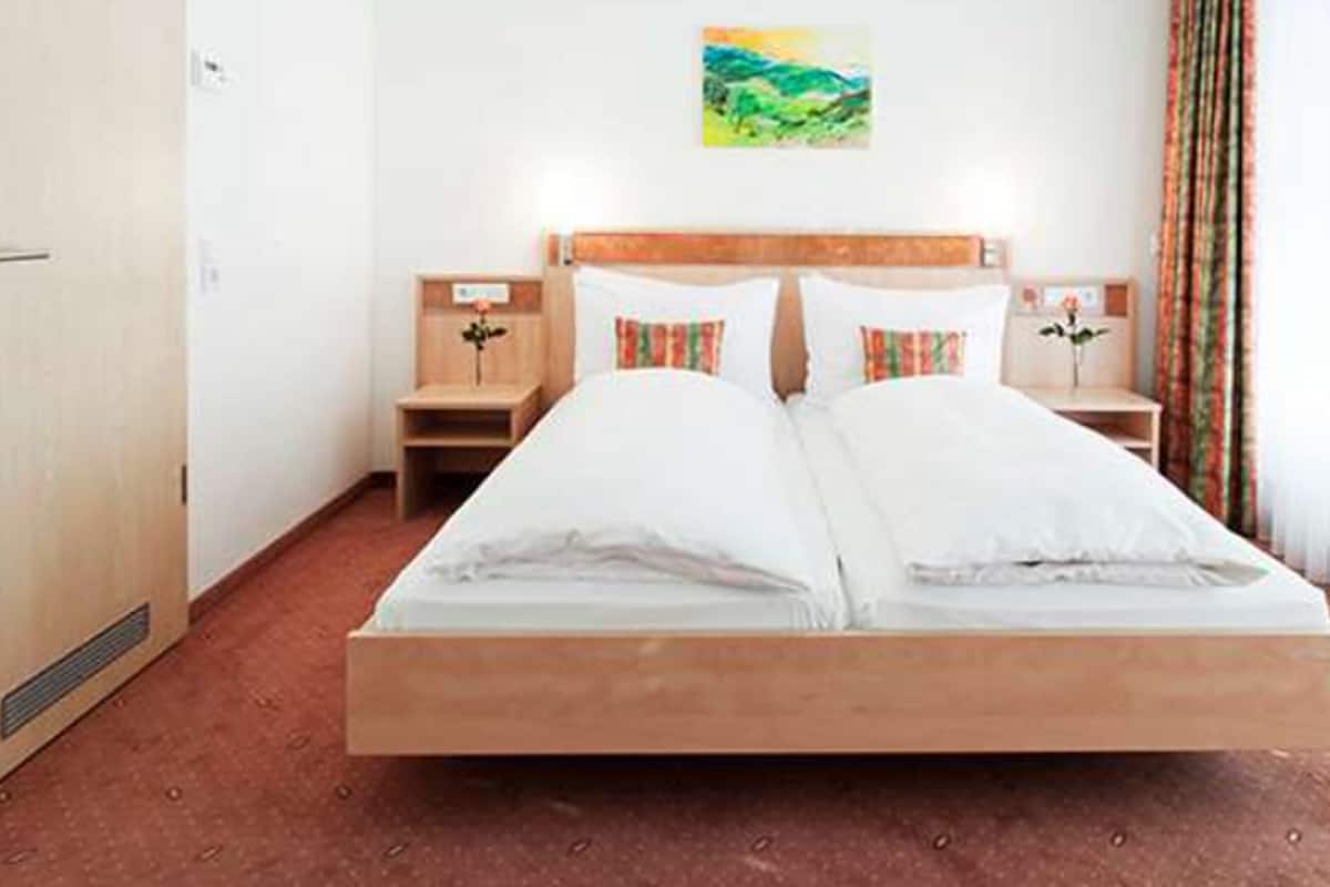 A hotel room with a wooden bed, two bedside tables, a nightstand, a painting on the wall, and a window with curtains.
