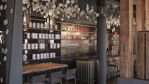 A modern bar with shelves of mugs and bottles, a wooden bar counter, and a seating area with chairs and a sofa.