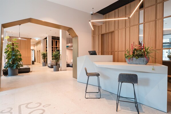 A modern reception area with a white reception desk, two bar stools, and potted plants.