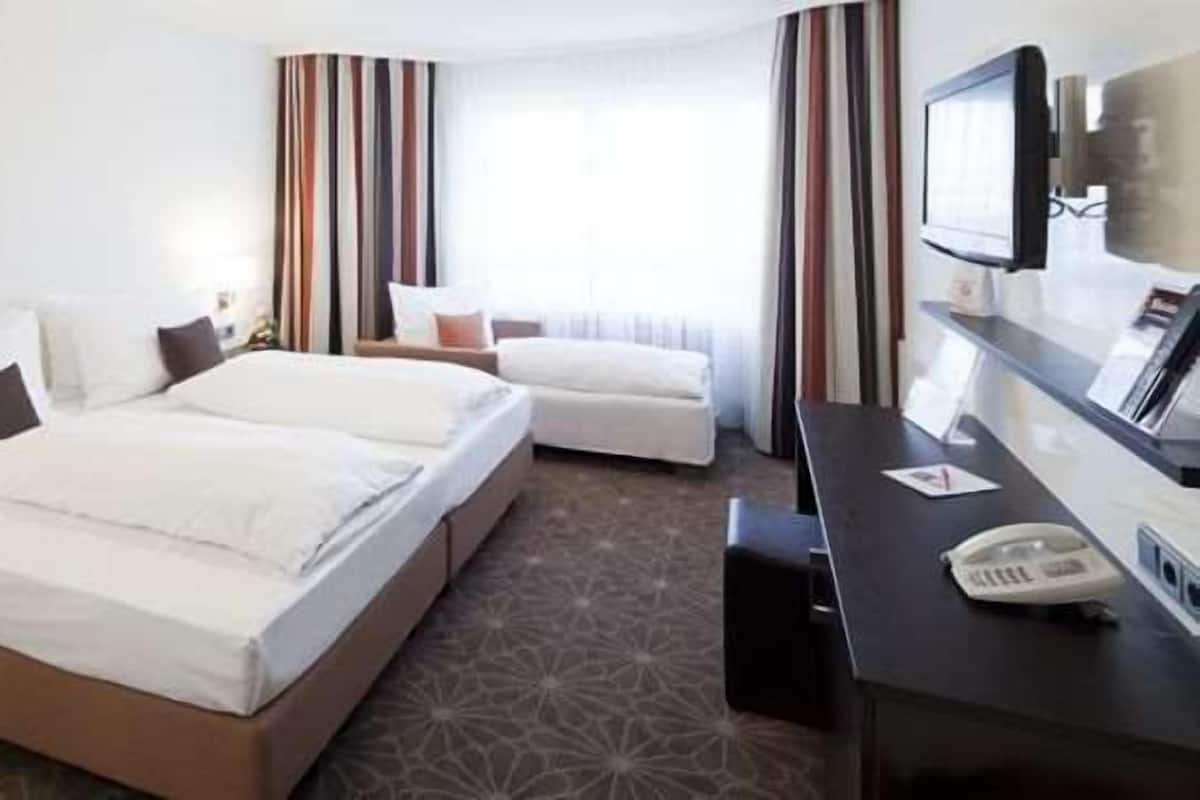 A hotel room with two beds, a desk with a telephone, and a TV.