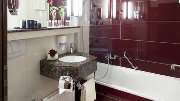 A modern bathroom with a white toilet, a sink with a marble countertop, a large mirror, and a bathtub with red tiles.