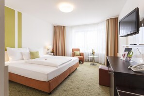 A hotel room with a large bed, a desk with a telephone, a television, and a chair. -  ZELLER's Quartier (Koenigsbrunn)